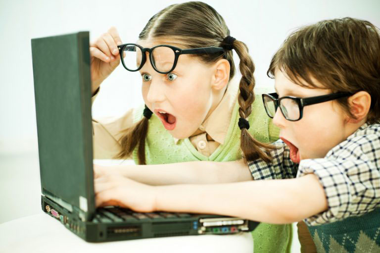 A boy and girl with glasses reacting excitedly to a laptop