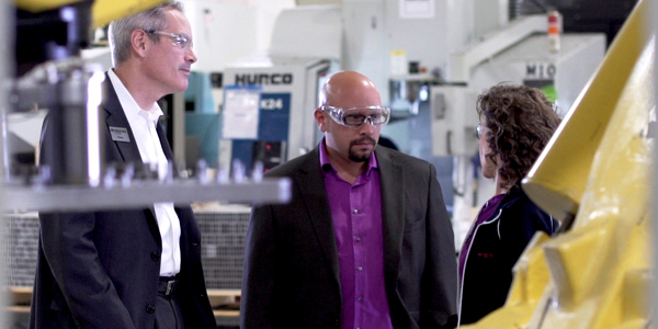 Two men and a woman with safety glasses on in an industrial setting
