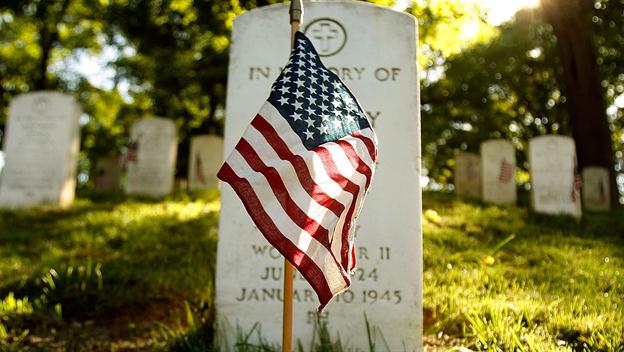 Small American flag in front of a tombstone on a sunny day