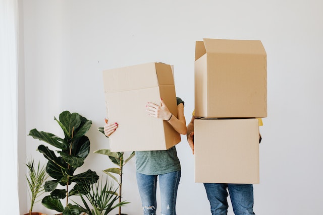 Two people holding cardboard boxes in a bare room