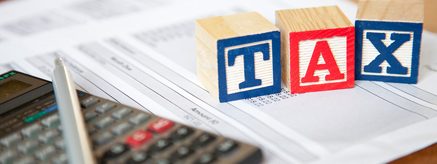 Calculator, pen, and tax documents with red and blue building blocks that spell out "tax"