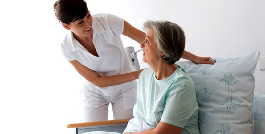 Medical professional leaning over and talking to an elderly lady in a medical bed