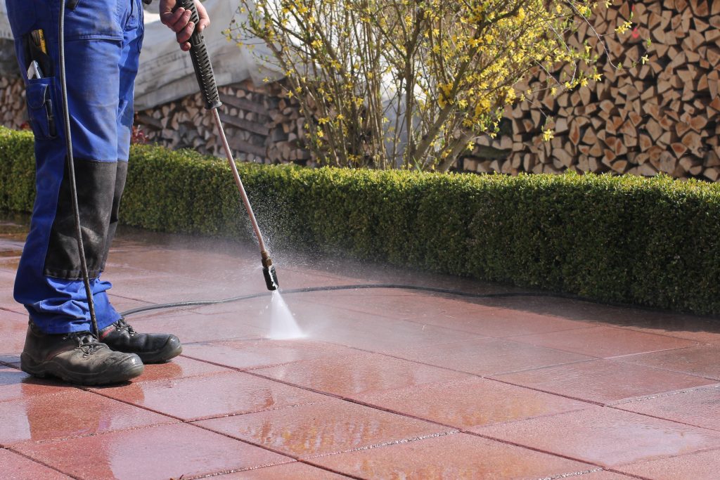 Close-up of a person powerwashing pavers on a patio with firewood piles in the background