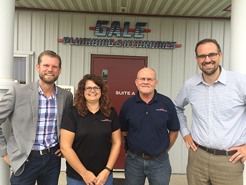 Three men and a woman smiling and posing for a picture in front of the Gale Plumbing and Hydronics business locations
