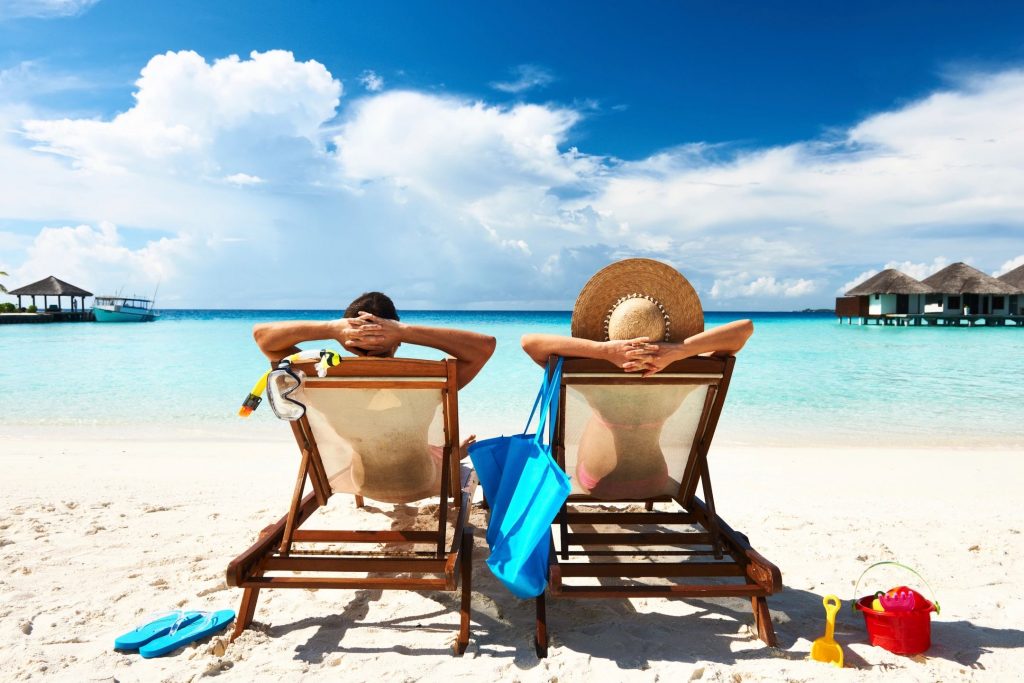 A man and a woman sitting in beach chairs in a tropical setting looking out over a beach shore