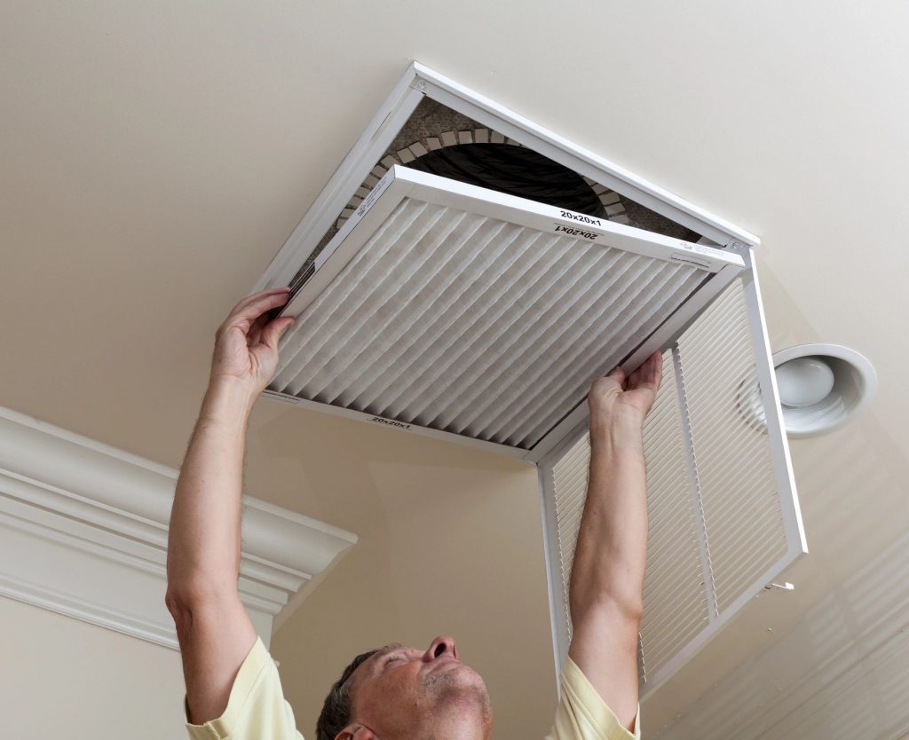 A man changing an air filter on an overhead vent for a forced air system