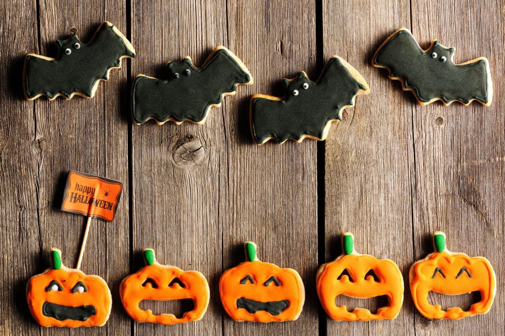 Four black bat cookies and five jack-o'-lantern cookies laid out on wooden slats