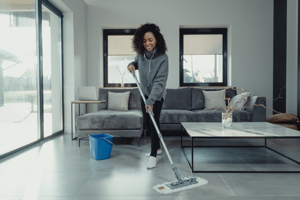 A woman listening to music while mopping the floor, smiling.