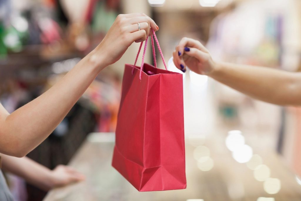 A woman handing a red gift bag to a customer in a store