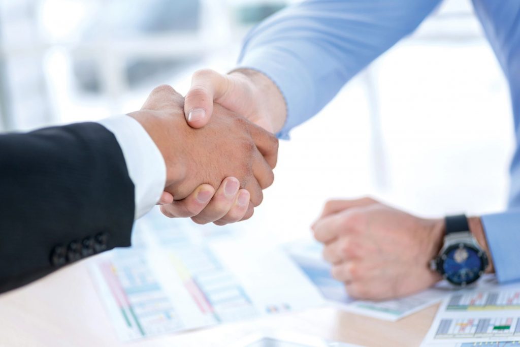 Close-up of two men shaking hands over a desk covered in spreadsheets