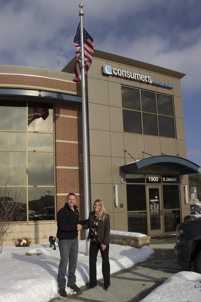 Man and woman shaking hands and smiling outside of a Consumers Credit Union office
