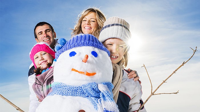 A family posing behind a snowman on a sunny winter day