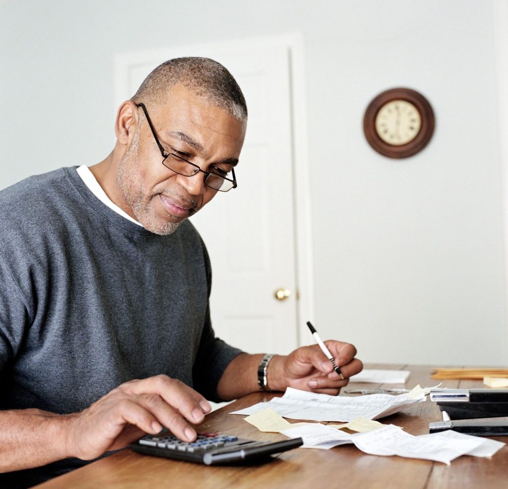 An older man balancing a checkbook with a calculator at a dinner table