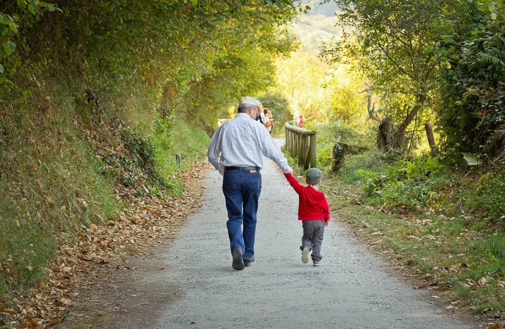 A grandfather walking and holding hands with his grandson along wooded path