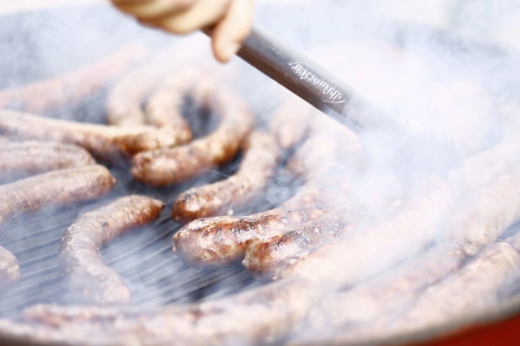 Close-up of someone grilling sausages with lots of smoke rising off of the grill
