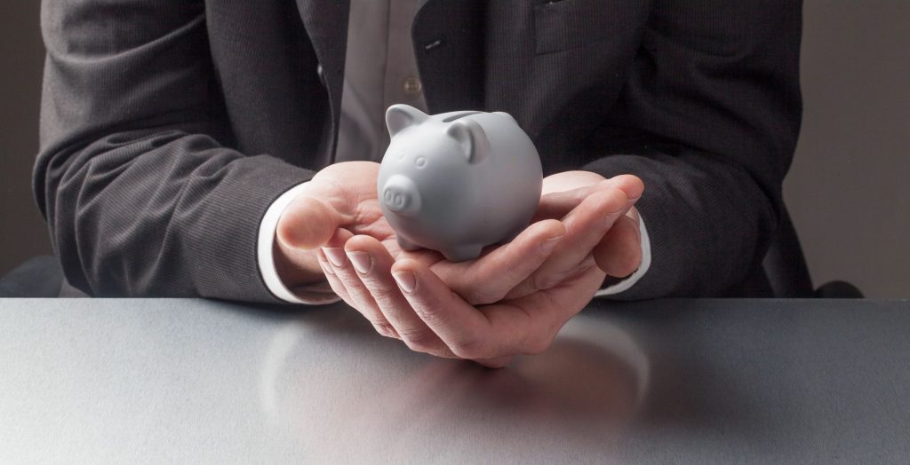 A man in a suit holding a grey piggy bank in his hands