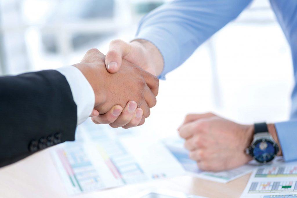 Close-up of a two men shaking hands over graphs and spreadsheets