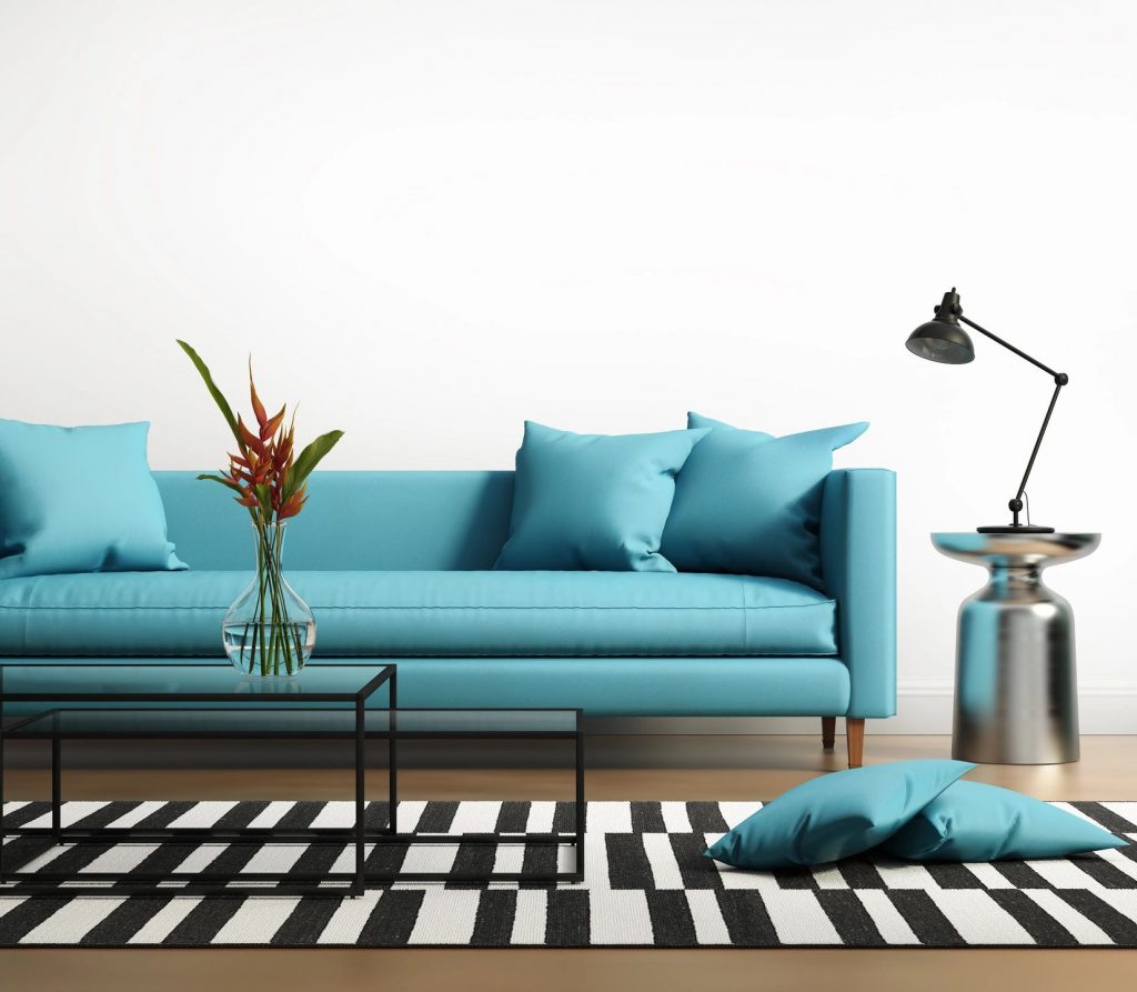 A turquoise couch with a glass coffee table next to a lamp with two pillows on the ground
