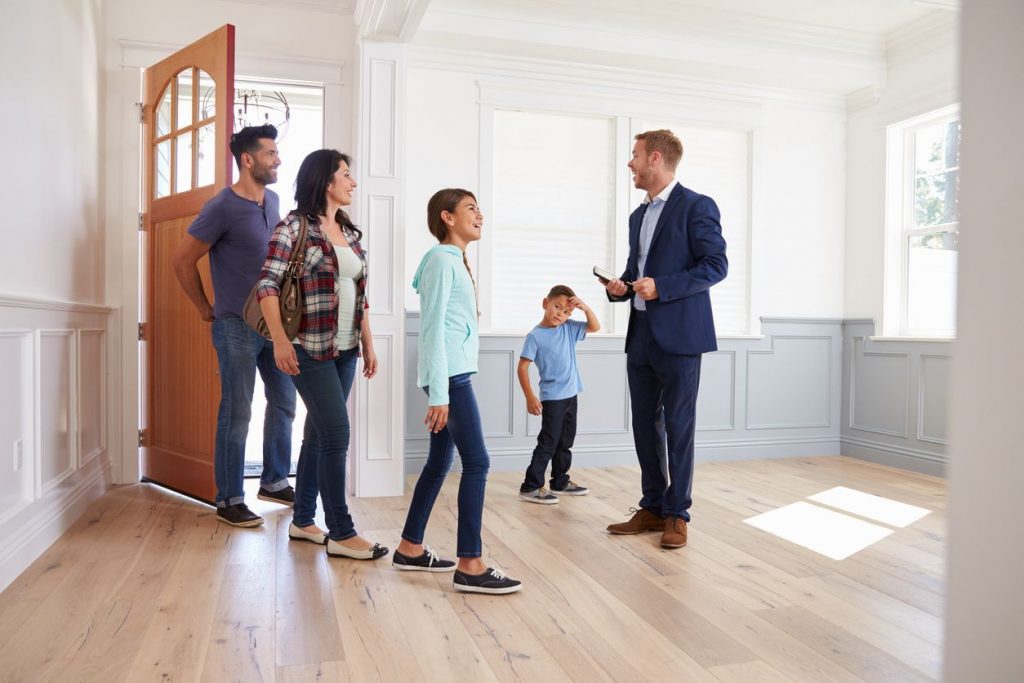 Family of four walking into an empty house with a real estate agent on a sunny day