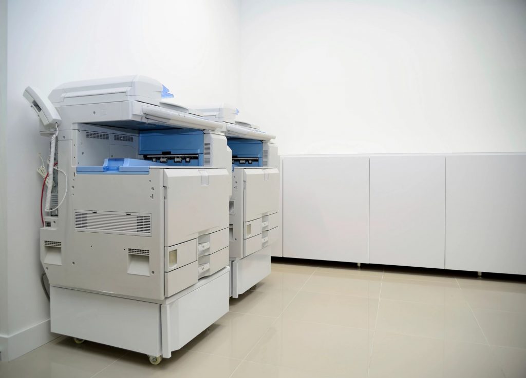 Two white photocopiers/fax machines in a white room
