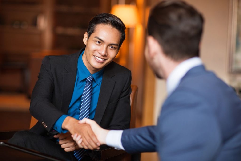 Two young men in suits shaking hands in an office