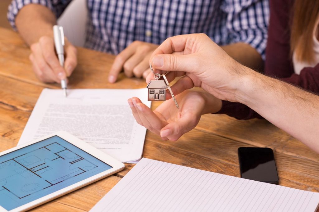 A couple signing a deed on a home while receiving a house key from the selling agent