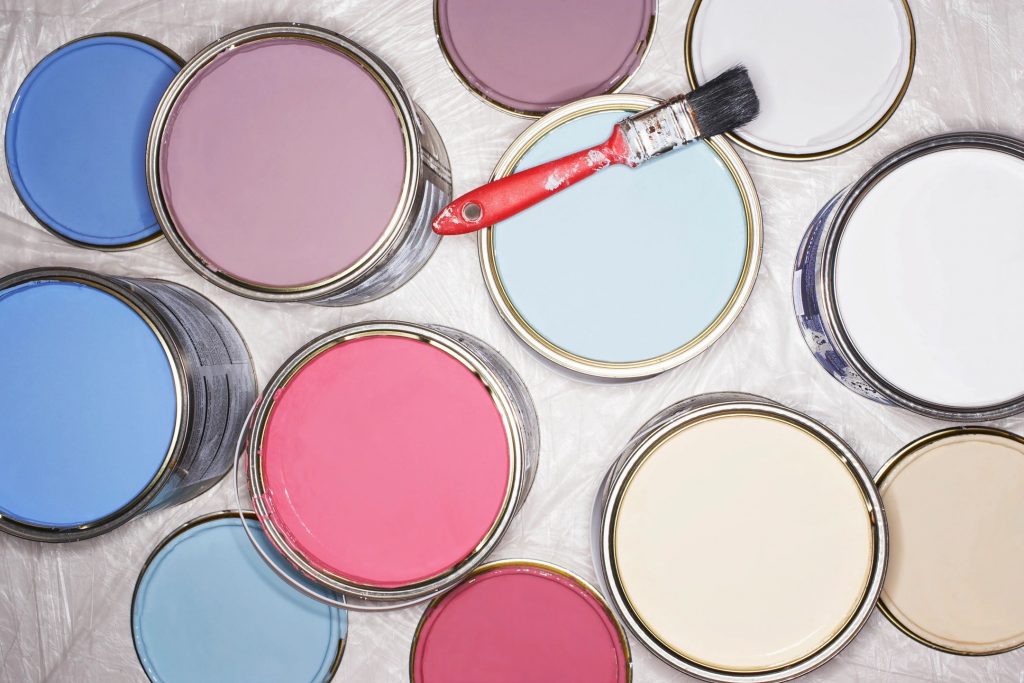 Many paint cans of red, blue, purple, and white open with a red paintbrush resting on one