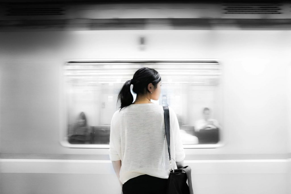A young lady with black hair and a white sweater standing in front of a moving train