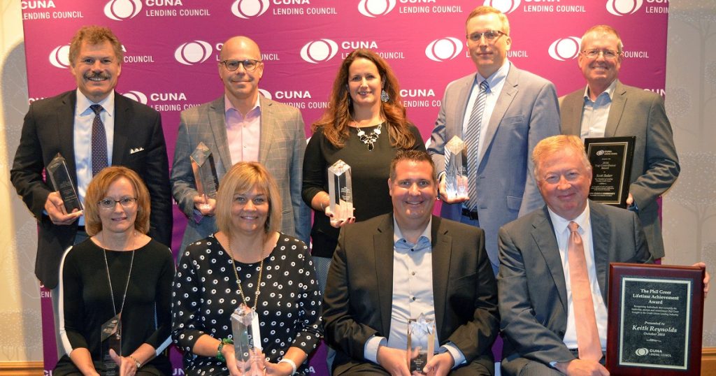 A group of men and women posing with awards in front of a CUNA Leading Council Step-and-Repeat