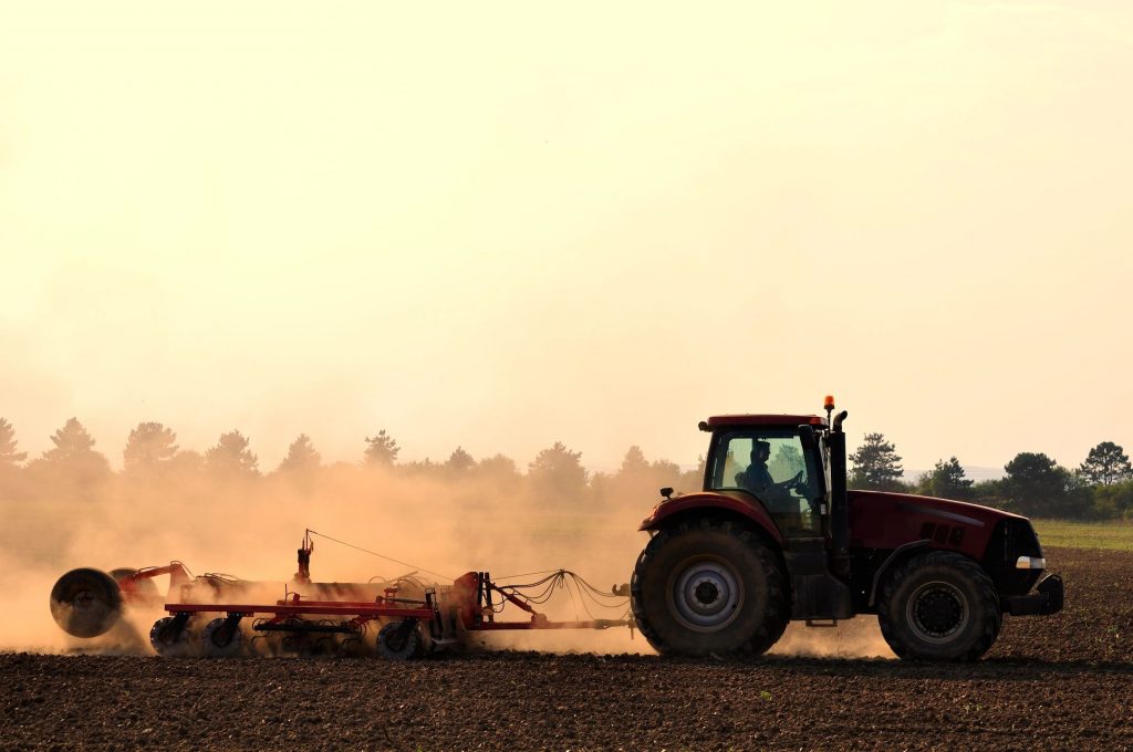 A tractor pulling a tillage attachment on the back kicking up dust on a farm
