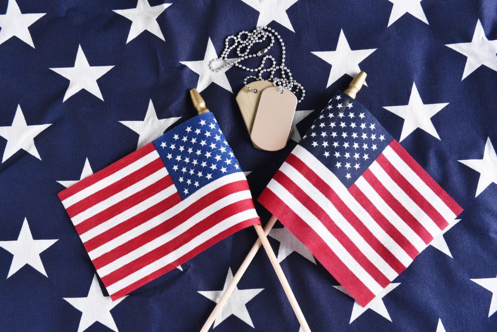 Two small American flags criss-crossed near a set of dog tags on the stars section of a larger American flag