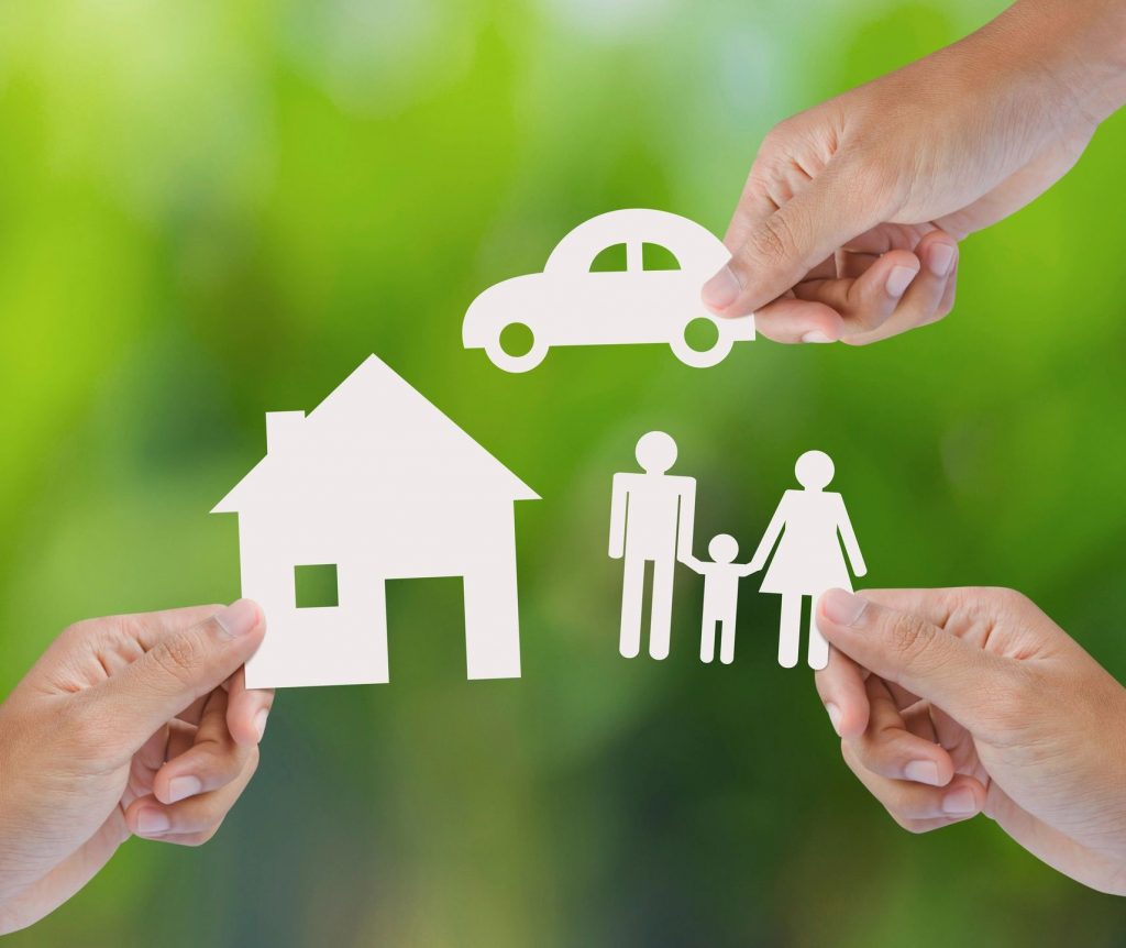 Three hands holding white cut-outs of an icon of a car, house, and a family