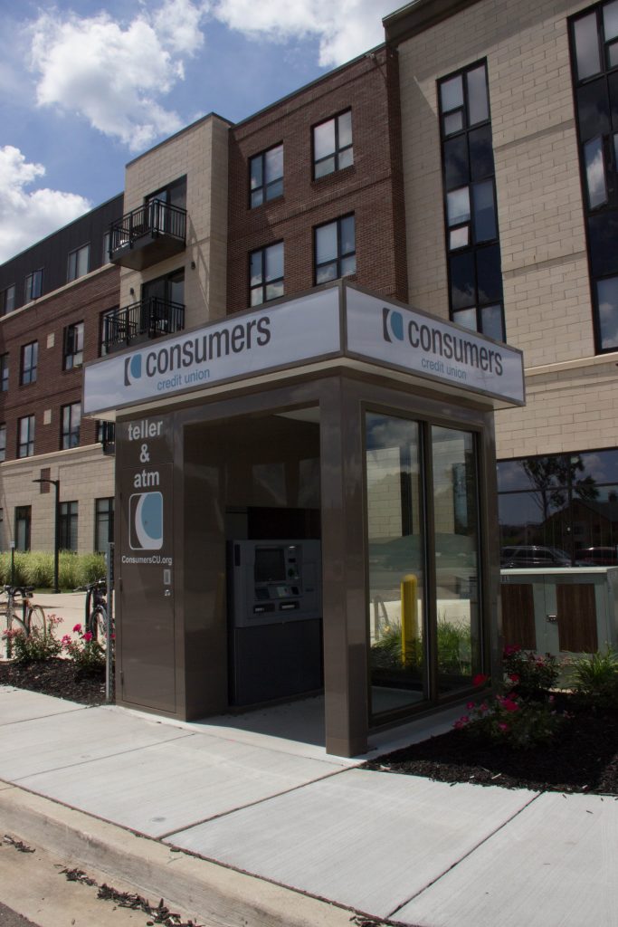 A brown Consumers Credit Union Teller & ATM kiosk outside of an apartment building