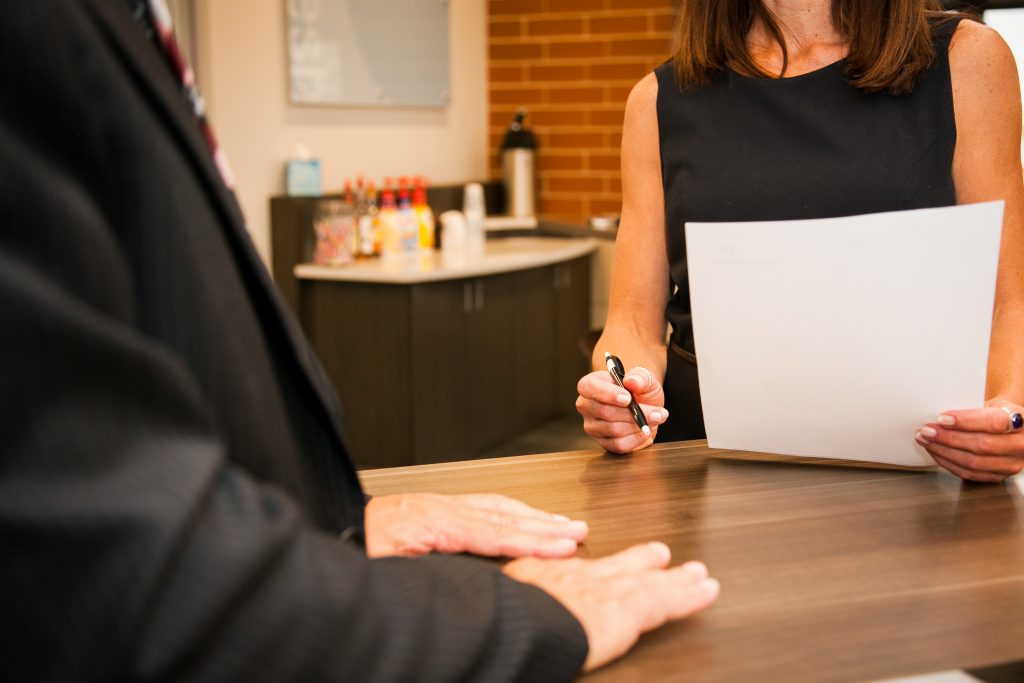 A woman holding a pen and paperwork across a standing height table in a cafe setting