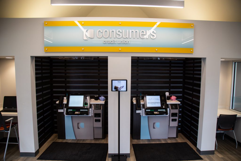 Two ATM kiosks underneath a yellow Consumers Credit Union sign