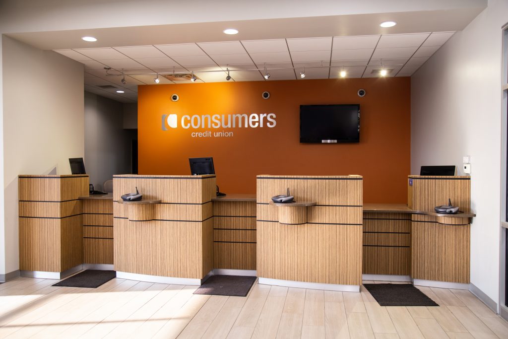 A Consumers Credit Union bank teller windows with an orange wall in the background