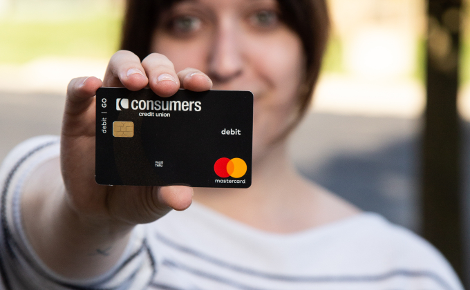 A woman holding a black Mastercard Consumers Credit Union debit card