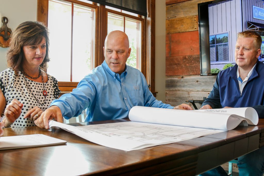 Two men and a woman sitting at a table with blueprints spread out on a table