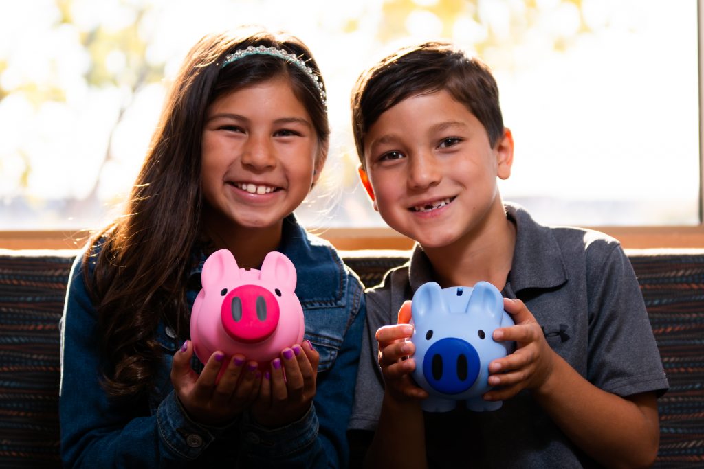 A young boy and girl smiling and holding piggy banks