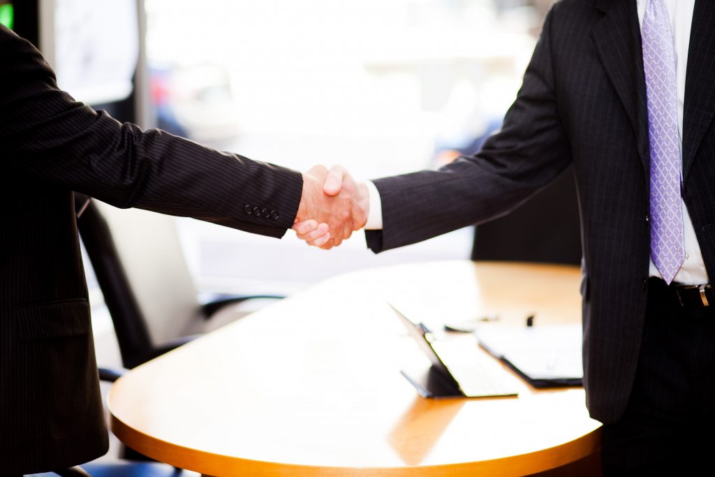 Two men standing and shaking hands in front of a table