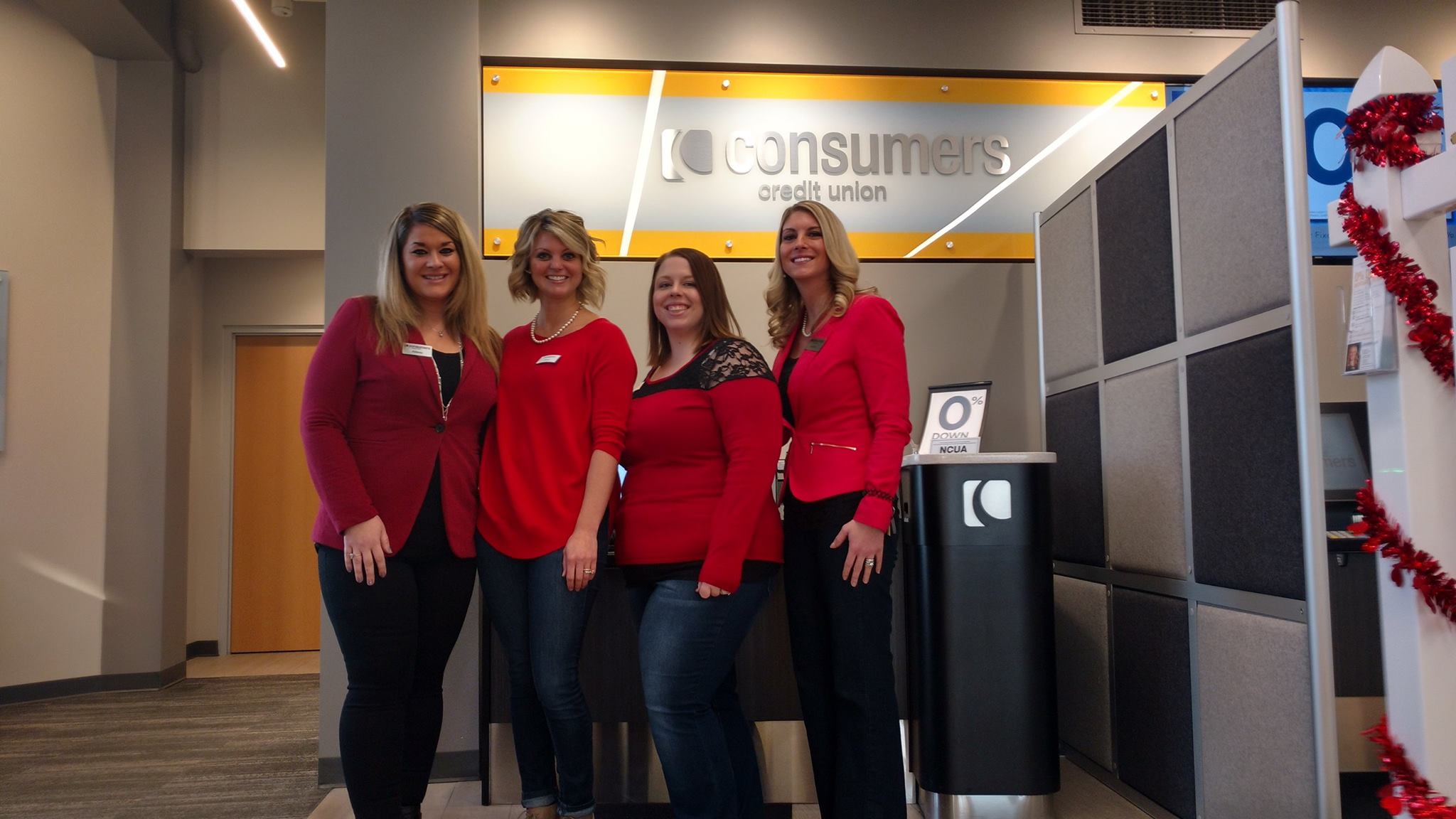 Four women in red smiling in front of an orange Consumers Credit Union sign