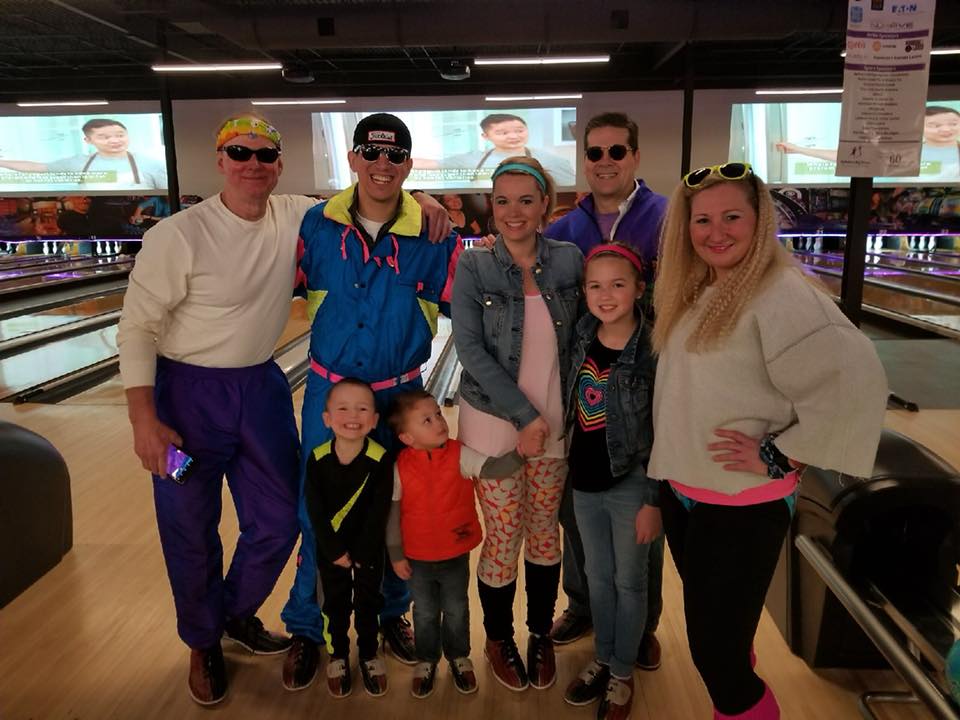 A group of people happily posing in front of bowling alley lanes
