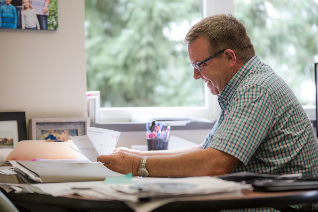 Man with glasses and a green plaid shirt sifting through paperwork on a desk
