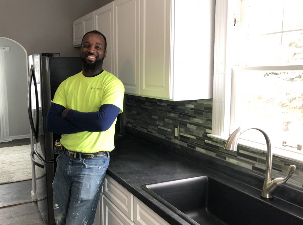 A carpenter leaning against a countertop in a kitchen smiling