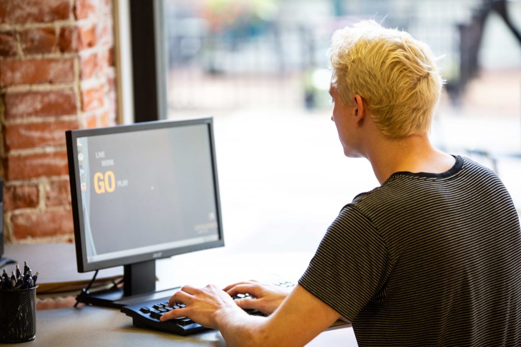 A young man with bleached blonde hair typing at a computer