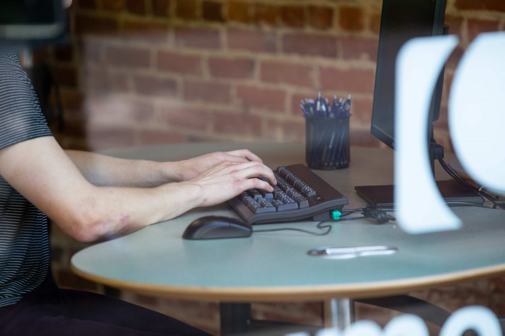 A man with a striped shirt typing on a keyboard and computer