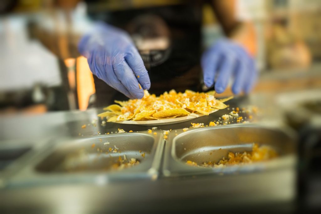 A person with blue latex gloves making nacho chips in a restaurant kitchen setting