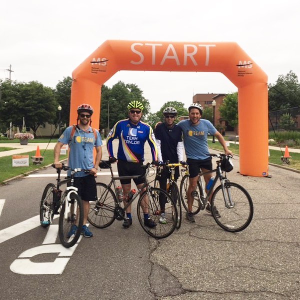 Four men on bikes standing in front of an orange Starting Point Arch