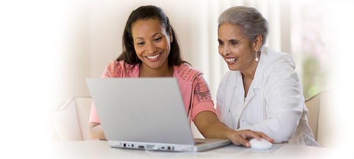 A smiling mother and daughter sitting at laptop on a table.