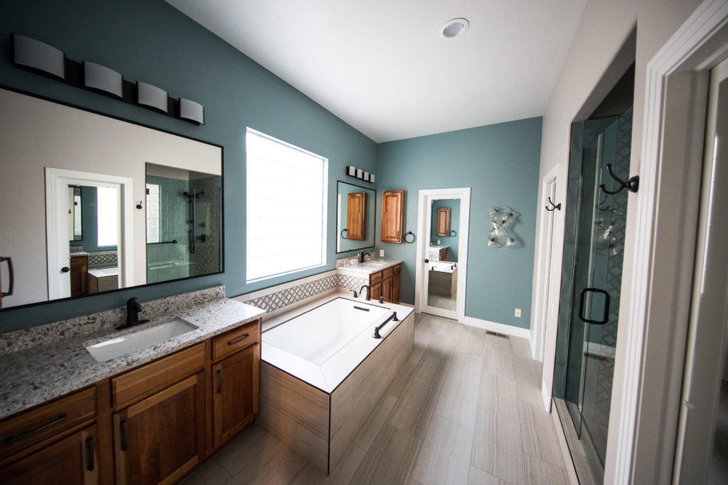 A large bathroom with a tub by a window across from a shower with glass doors
